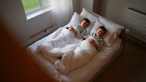 two young boys smiling while lying in bed in their pajamas