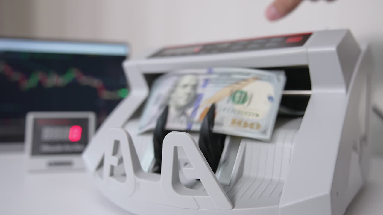 A hand switches on money counting machine. A wad of hundred dollar bills is being put into equipment for cash calculation. Close up. Blurred backdrop.