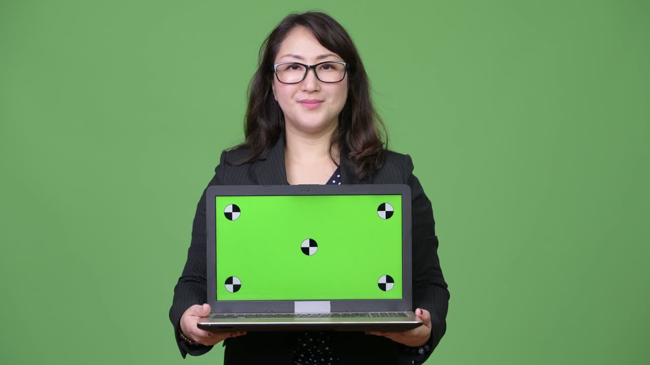 una hermosa mujer de negocios asiática madura mostrando una computadora portátil contra un fondo verde