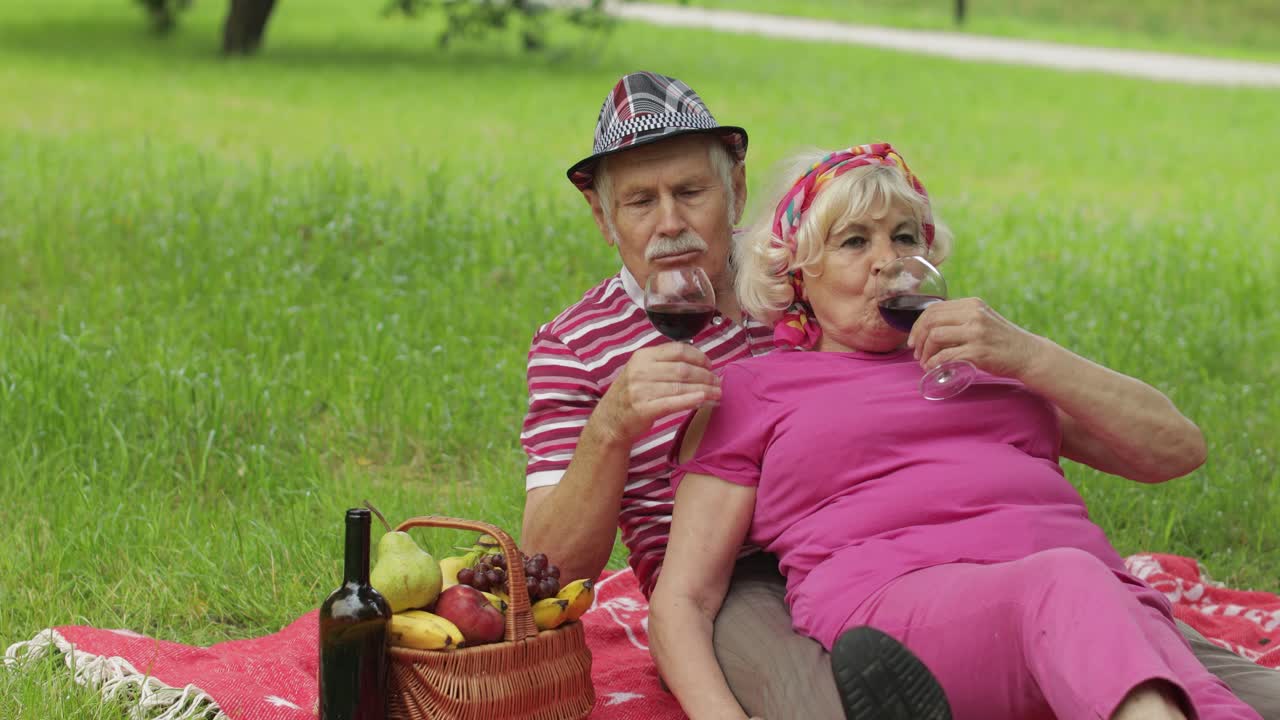 주말에 공원에서 가족 피크닉을 하는 활동적인 노인 백인 부부는 담요 위에 앉아 와인을 마신다.