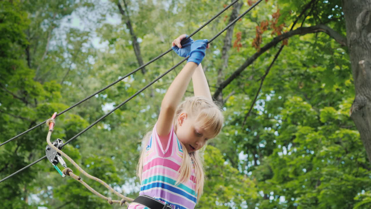 una chica valiente se mueve a lo largo de las cuerdas entre los árboles usa una cuerda de seguridad