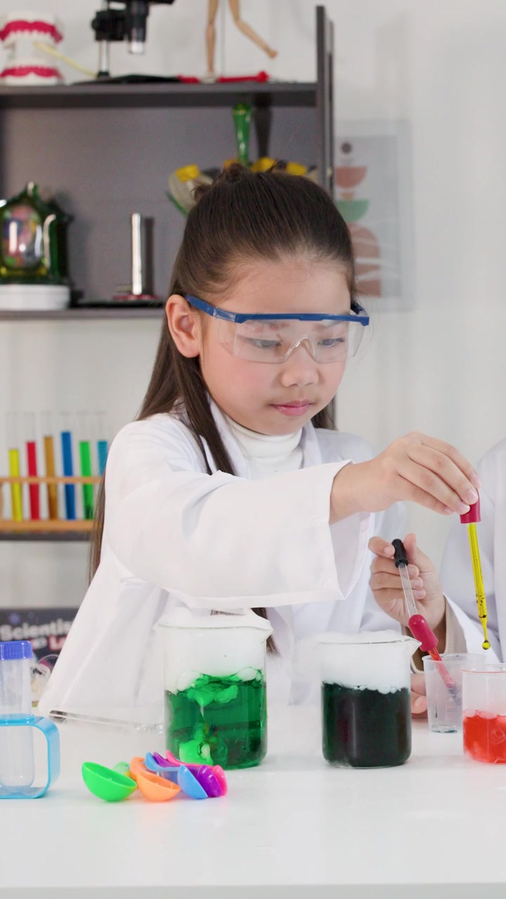 Gadis muda Asia mengenakan kacamata pengaman menggunakan pipet selama percobaan sains di kelas.