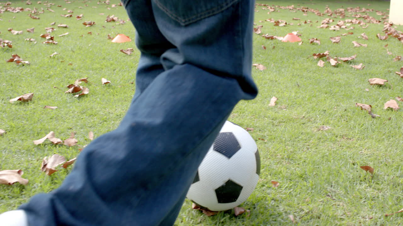Happy african american mother and son playing football in garden, in slow motion