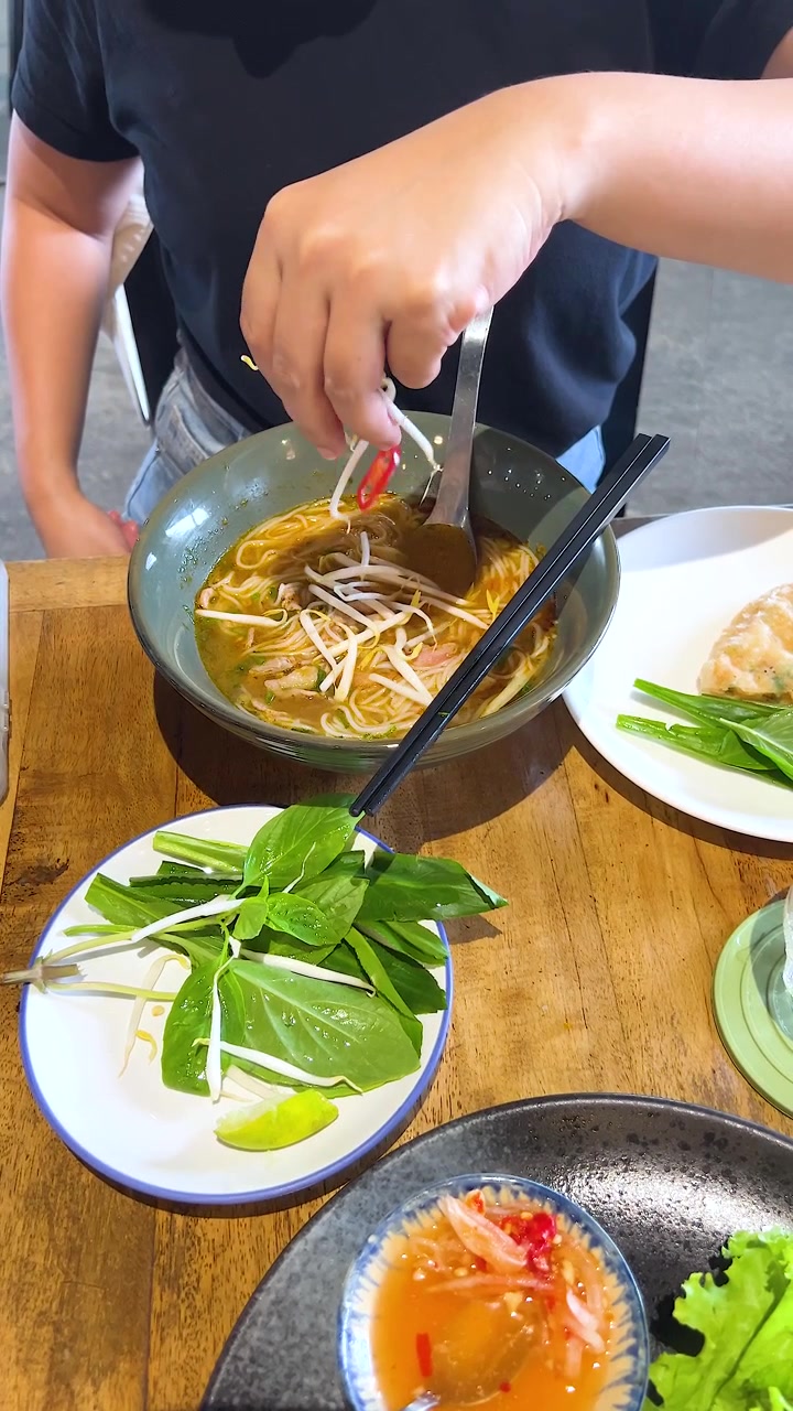 Một người thêm rau thơm tươi và chanh vào tô phở Việt Nam tại một nhà hàng, giúp món ăn thêm đậm đà hương vị.