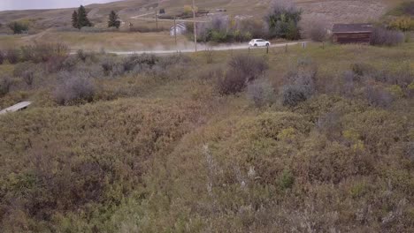 Panning-aerial-as-white-car-drives-romote-dirt-road-in-rural-badlands