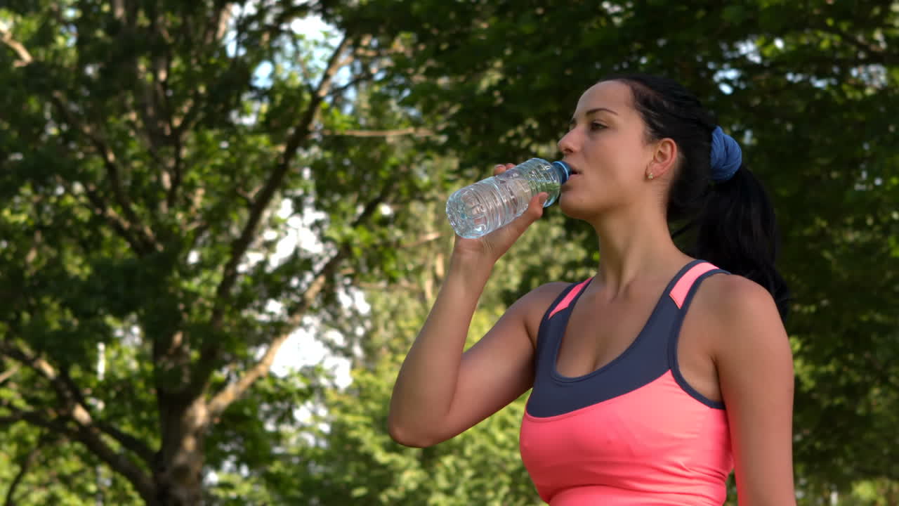 una morena en forma bebiendo de una botella de agua.