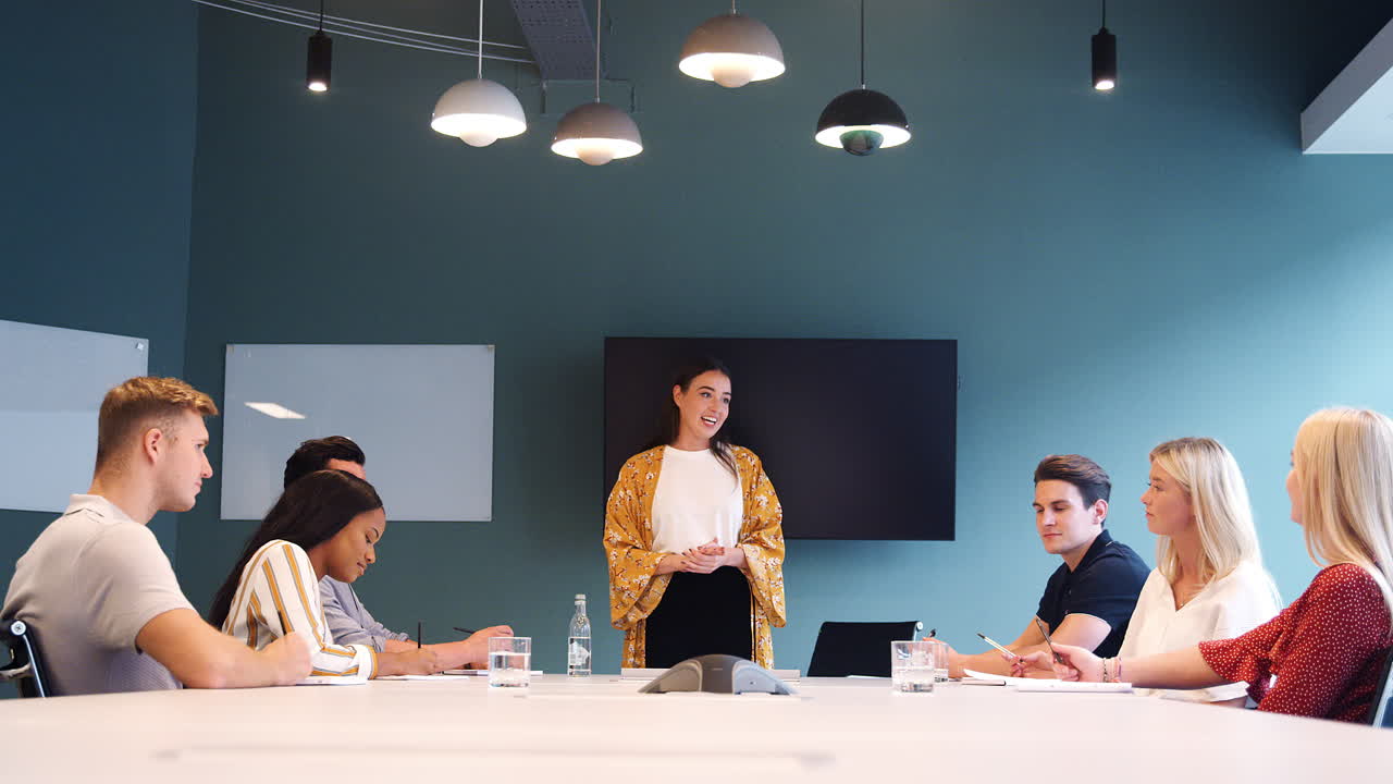 mujer de negocios dirigiéndose a un grupo de candidatos reunidos alrededor de una mesa en el día de evaluación de reclutamiento de graduados