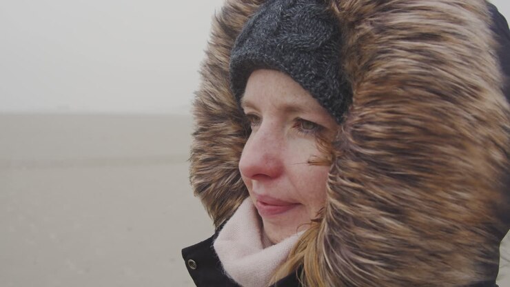 Young woman standing in the wind of a barren landscape, protected from the freezing cold with a fur hood - Slow Motion