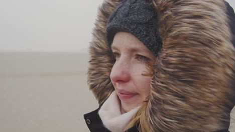 young woman standing in the wind of a barren landscape, protected from the freezing cold with a fur hood - slow motion