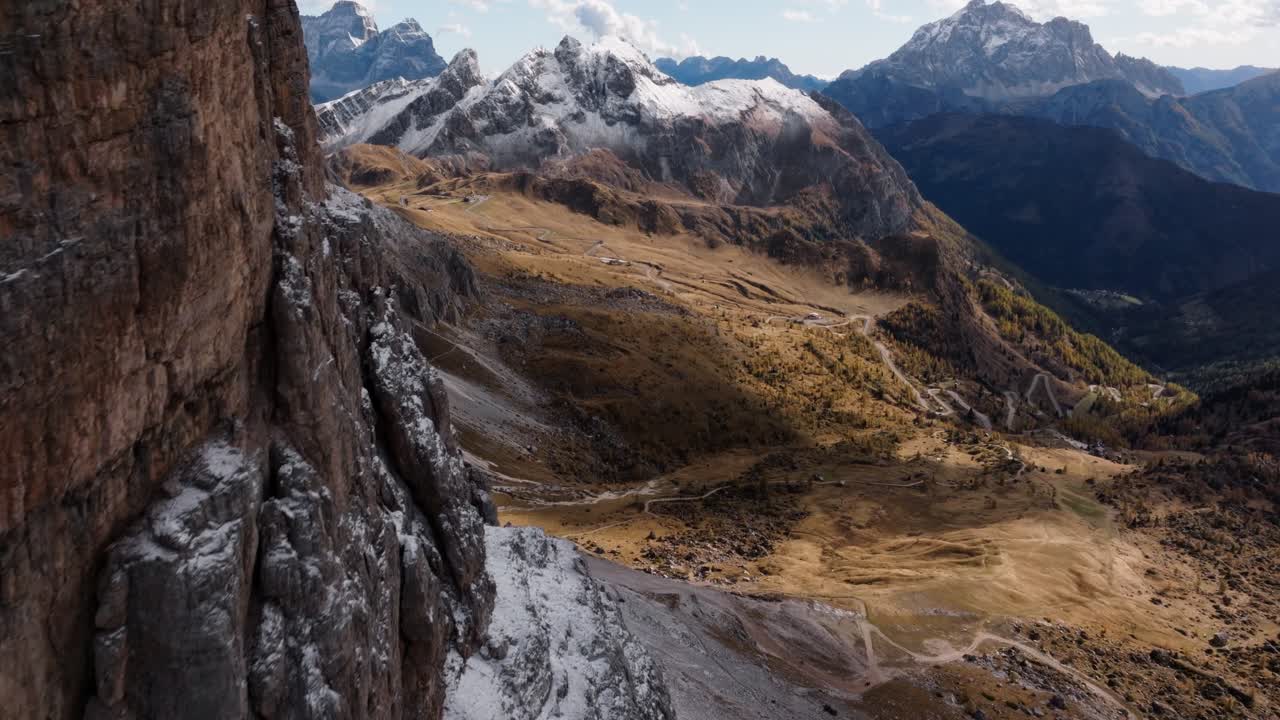 Drone clip of passing Monte Averau in the Italian Dolomites and revealing the valley which is full of colourful trees, while Passo Falzarego is also visible