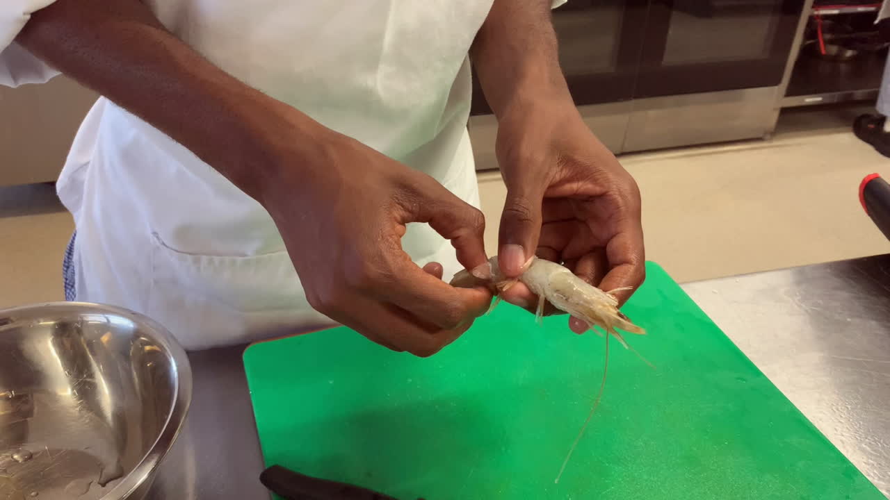 Young chef in commercial kitchen removes shell from large prawn