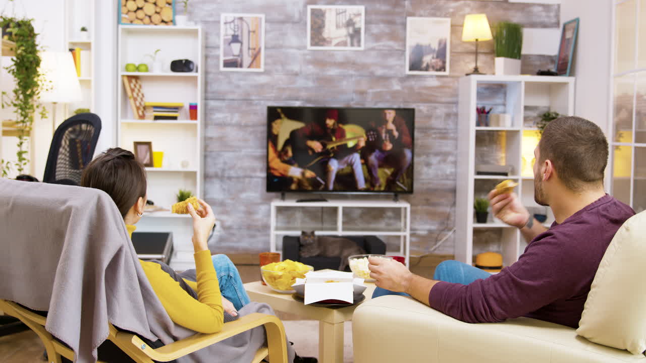 A couple is eating while watching TV in the living room