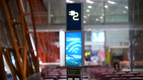 at beijing international airport, an illuminated charging station sign near the boarding gate allows passengers to power up electronic devices like smartphones and laptops.