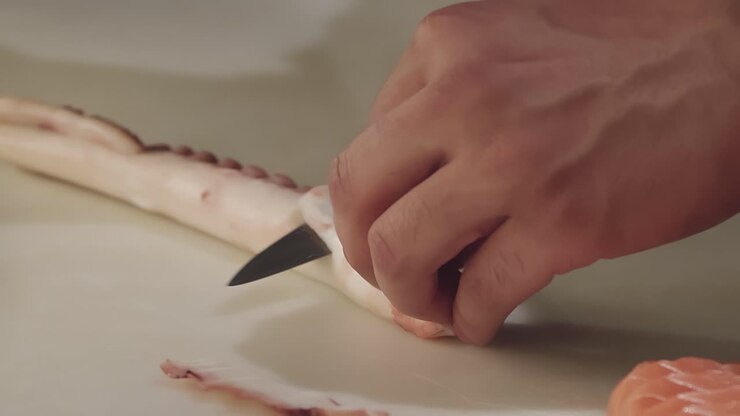 A chef carefully slices an octopus tentacle with a knife in a restaurant kitchen
