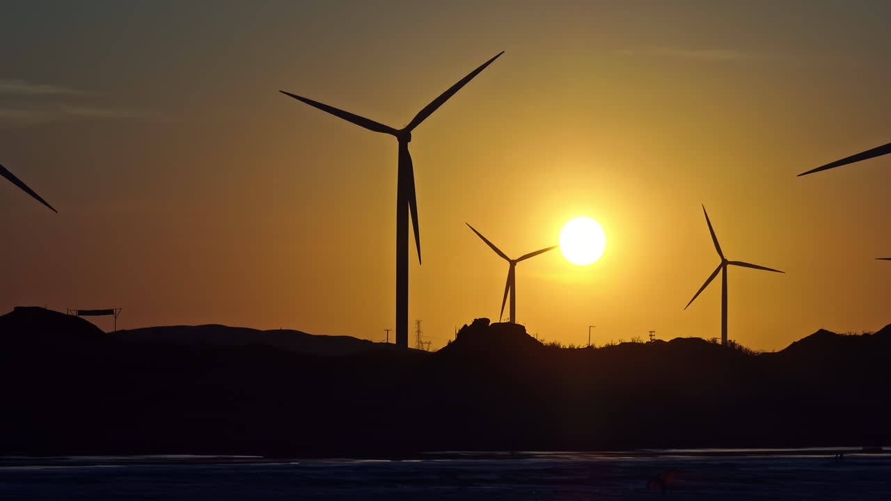 Long lens drone shot of backlit windturbines and kites on a beach in Brazil during sunset
