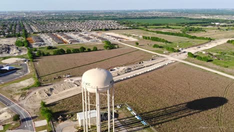 Flying-over-a-water-tower-and-ground-tank-towards-a-new-large-roadway-being-constructed-in-the-country-near-some-new-housing-sub-divisions