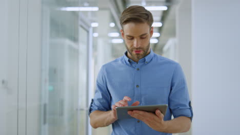 Joyful businessman using tablet in office. Business man working device indoors.