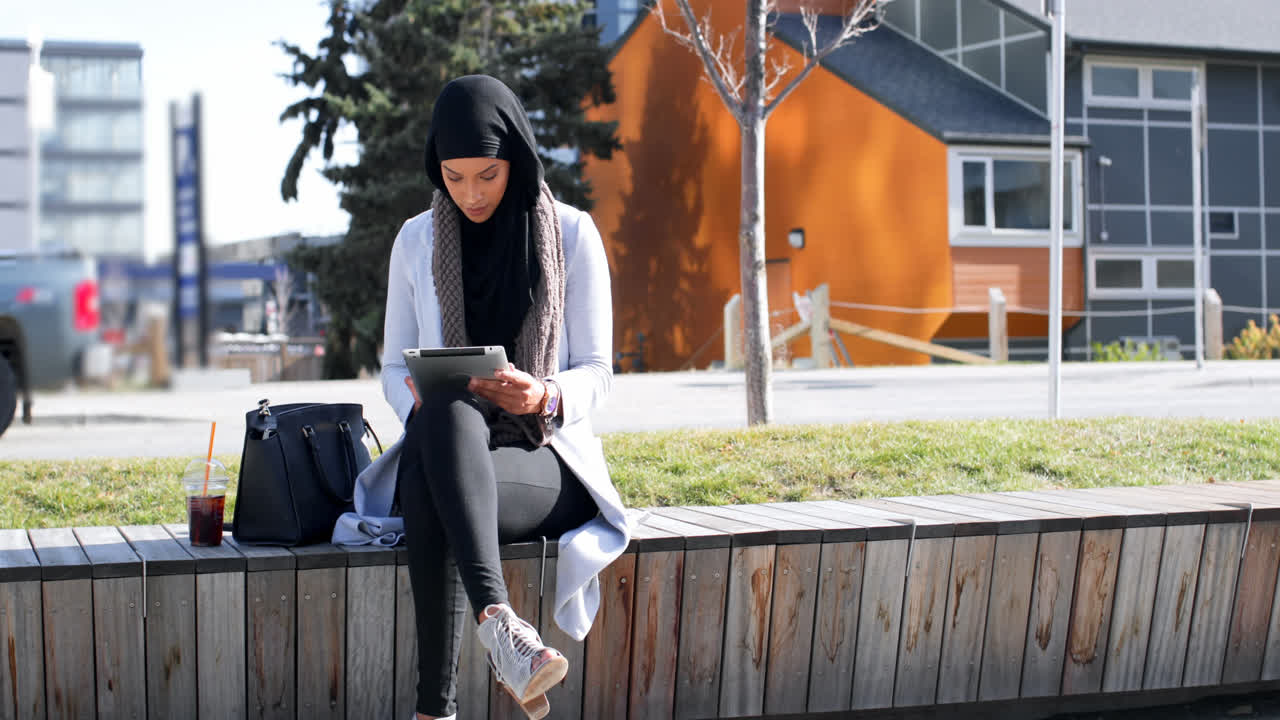 Front view of young Asian woman in hijab using digital tablet in the city 4k