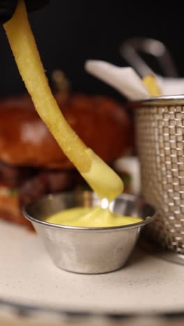 hand dipping french fries in sauce with burger