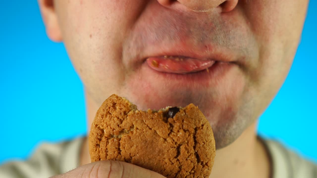 hombre mordiendo y comiendo galleta de chispas de chocolate. primer plano de la mitad inferior de la cara masculina, comiendo comida dulce