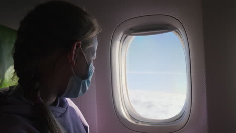 un niño con una máscara de protección mira a través de la ventana de la aeronave