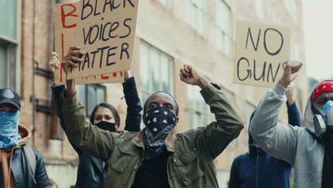 african american man yelling with arms up and holding a lack voices matter" signboard in a protest with multiethnic group of people in the street"