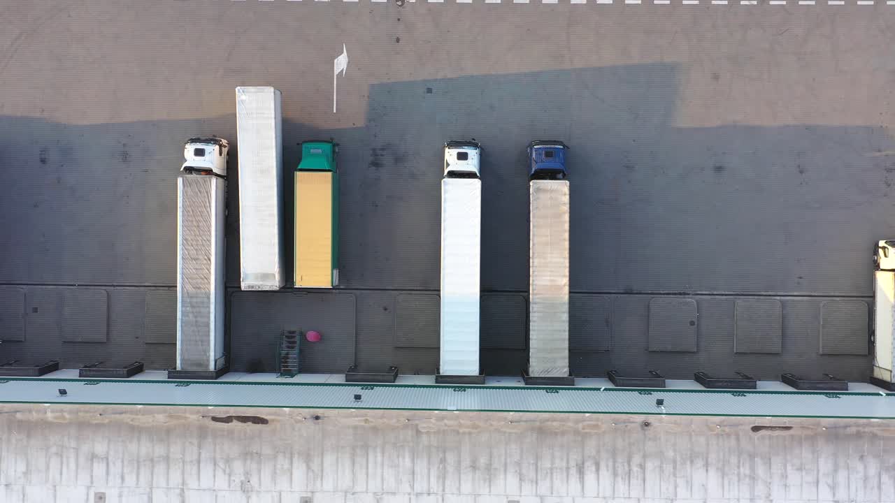 많은 트럭이 상품을 하역하고 있는 산업 창고 보관 건물 적재 구역을 떠나는 세미 트레일러가 부착된 트럭의 항공 샷