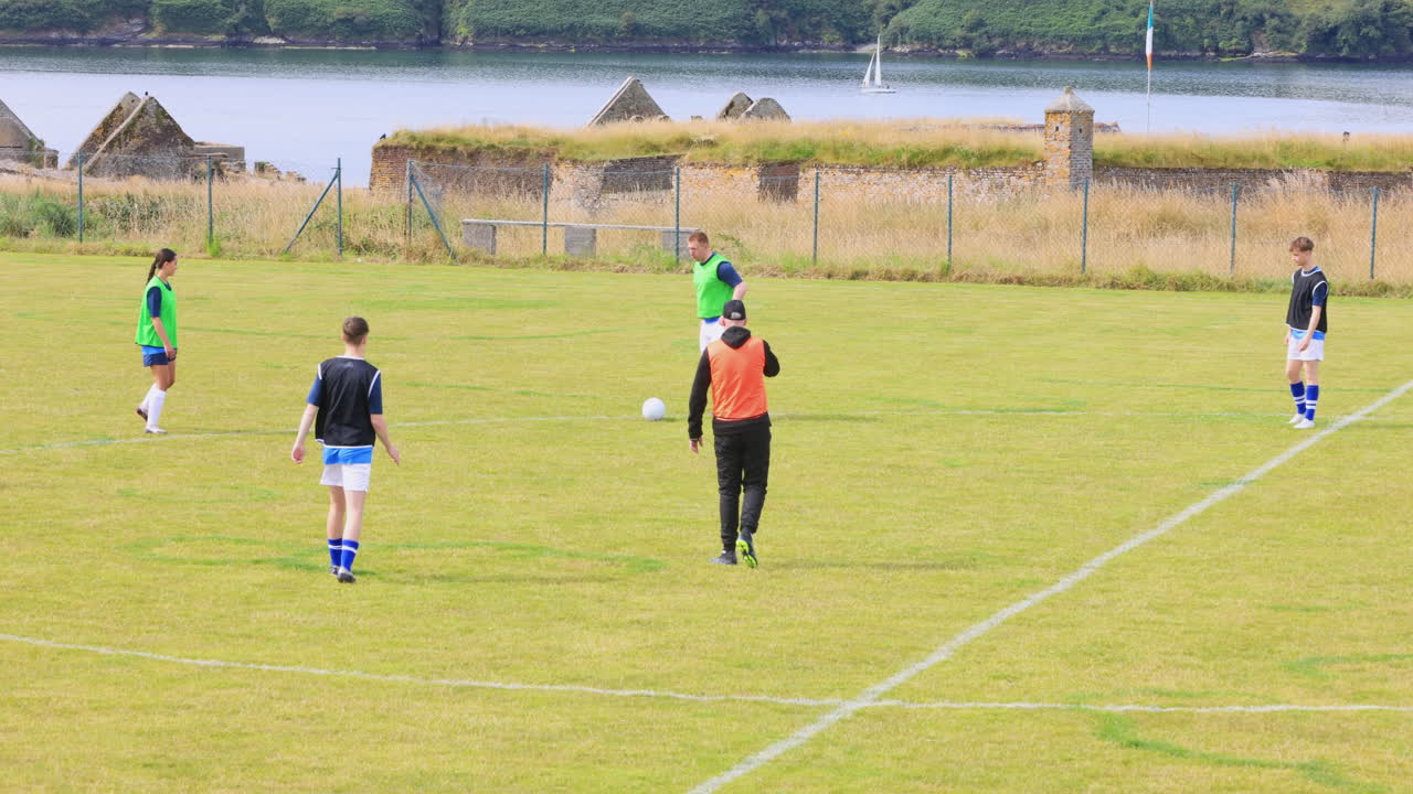 Male and female soccer players playing soccer, passing and running after ball with coach on pitch