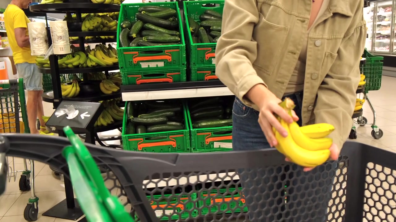 Giovane donna che seleziona banane al supermercato
