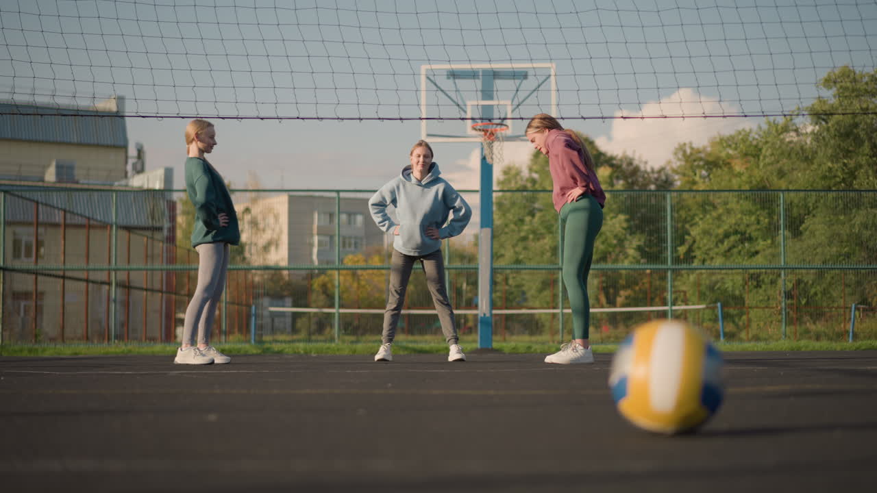 야외 스포츠 경기장에서 스포츠 드레스를 입고 허리 회전 운동을 수행하는 젊은 운동 선수, 배구가 전면에 보이며 운동은 유연성과 힘 훈련에 초점을 맞추고 있습니다.