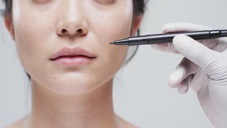 asian woman with dark hair and hand in white glove holding marker on grey background, slow motion