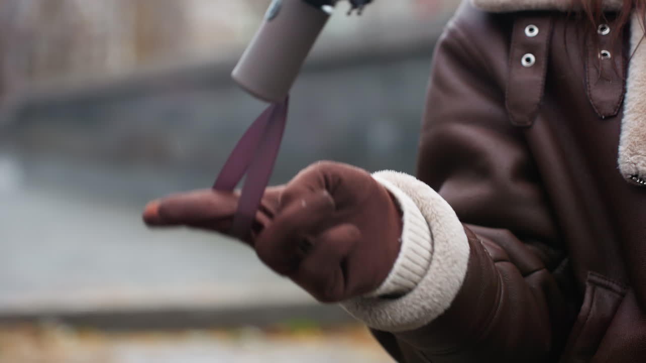 Close up shot of person hand in brown glove and shearling jacket playfully twirling umbrella outdoors on chilly autumn day with soft blur of city background and fallen leaves creating cozy atmosphere