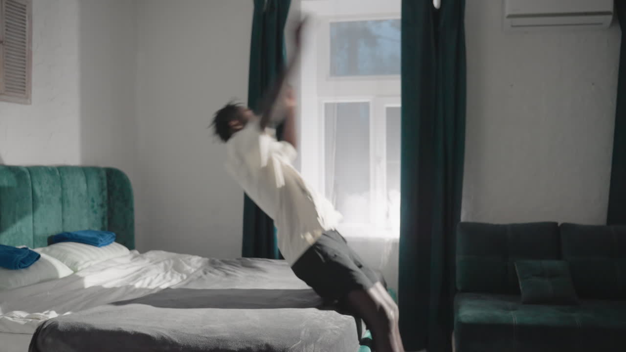 Person in white shirt standing near bed, holding a bag, modern bedroom with green velvet headboard, soft natural light streaming through window, calm morning atmosphere, peaceful home space