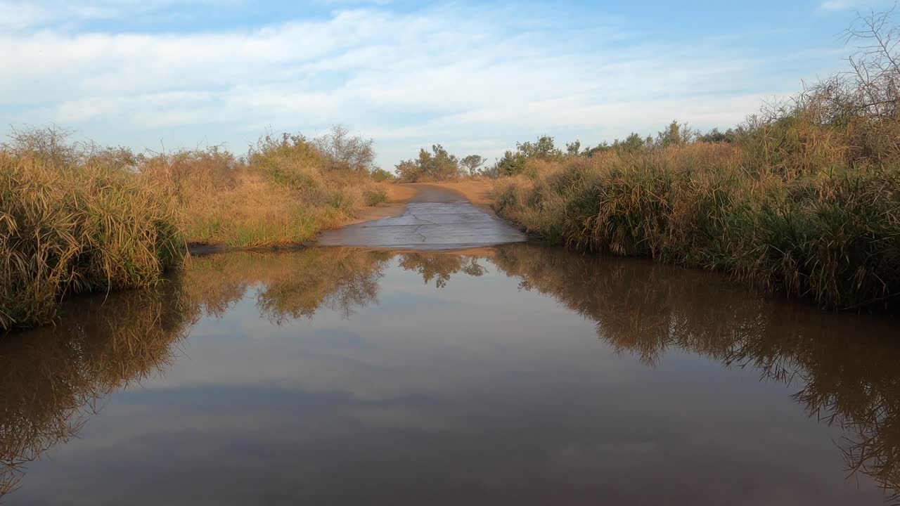 pov de un vehículo que conduce lentamente hacia y a través de un puente de bajo nivel con agua de lluvia en