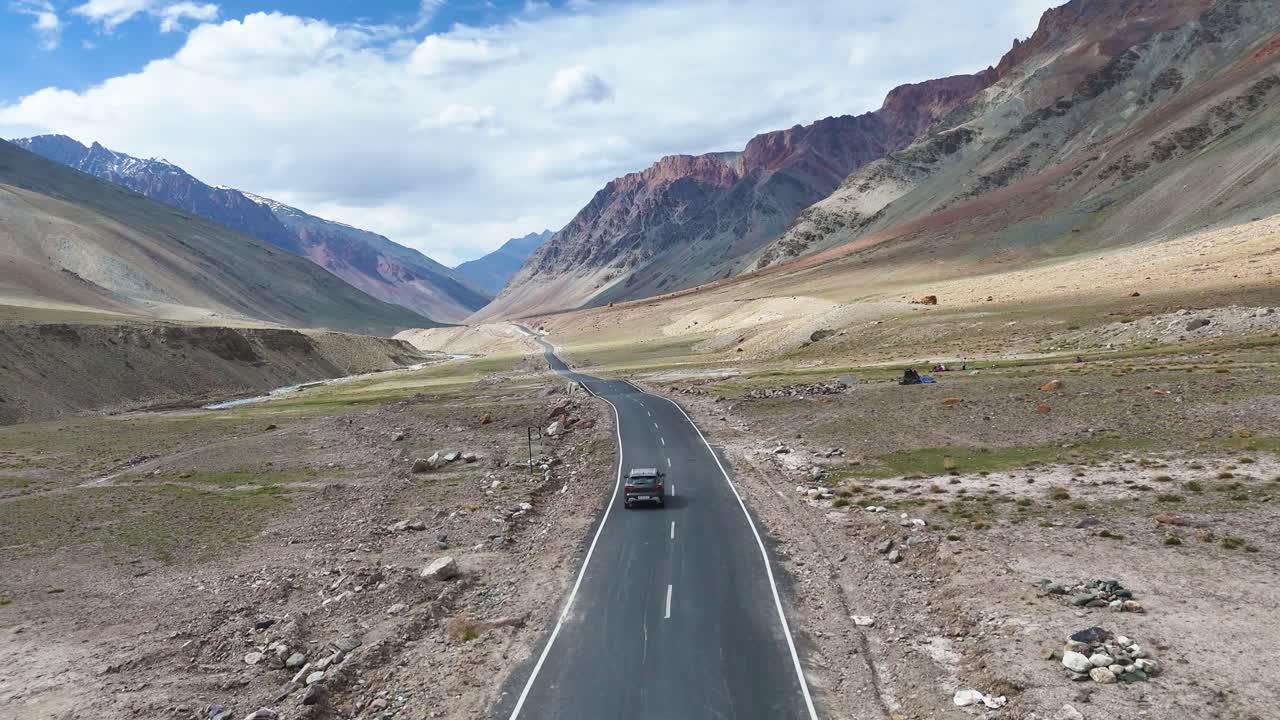 Aerial drone shot following a car driving through Ladakh’s remote mountain landscape on a straight highway.