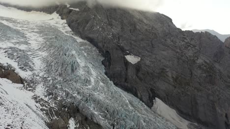 Aerial-shot-panning-up,-revealing-a-big-ice-and-snow-covered-glacier-on-top-of-a-mountain-in-Switzerland