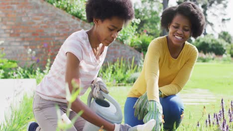 Portrait-of-smiling-african-american-mother-and-daughter-gardening-together-in-sunny-garden