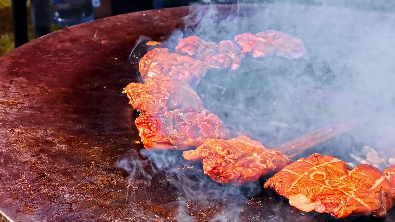 Daging yang diasinkan mendesis di atas panggangan barbeku panas besar dengan asap mengepul, menangkap tekstur berair, suasana jajanan kaki lima, dan cita rasa kuat dalam adegan memasak luar ruangan yang autentik