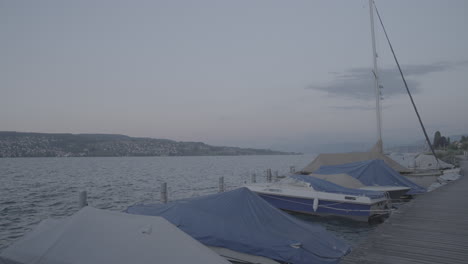viaje filmado en un muelle de madera observando el lago de zúrich con barcos en primer plano durante la puesta de sol en cámara lenta y montañas en el fondo y ondas en el registro de agua