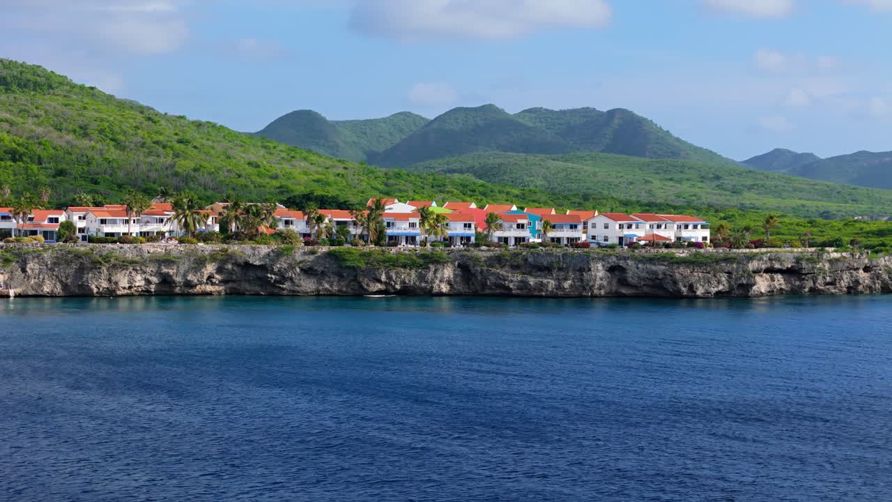 Edifici con tetto arancione e facciate blu e bianche si affacciano sulle scogliere tropicali del Mar Caraibico a Curaçao