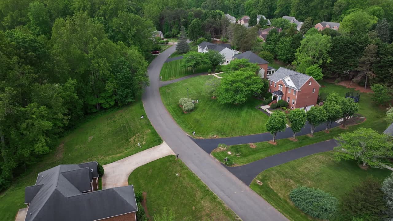 Aerial view of an American neighborhood featuring classic brick homes with gabled roofs, large windows, and spacious yards. The colonial-style architecture reflects elegance and traditional design.