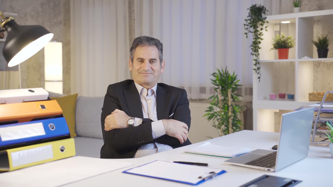 exitoso y motivado hombre de negocios maduro mirando a la cámara en la oficina de casa y sonriendo con los brazos cruzados.