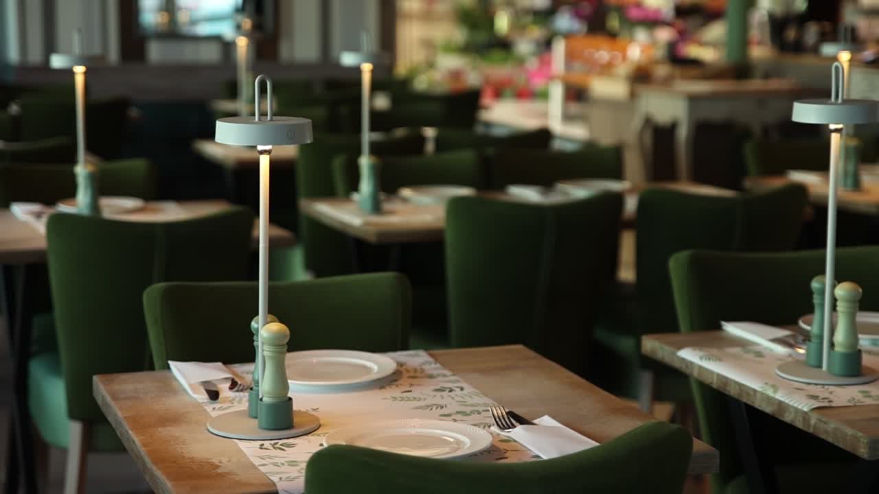 Tomma restaurangbord dukade med moderna lampor och gröna stolar
