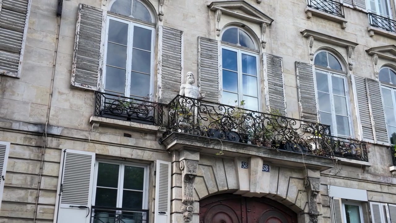 Inquadratura dal basso di un edificio storico parigino in pietra con persiane e statue classiche