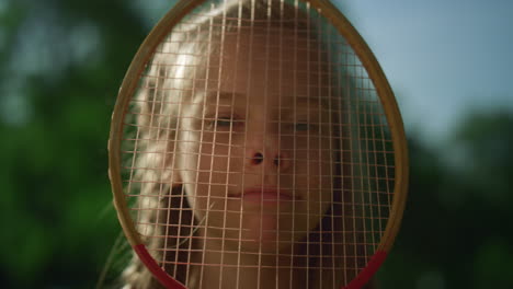 joyful little kid making funny face with badminton racket. girl pressing nose