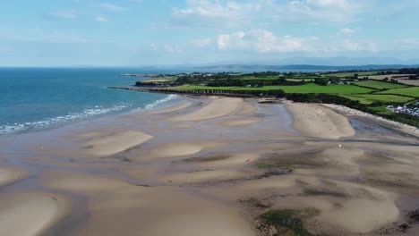 amazing cinematic drone clip of over the green pasture and the beachhead and waves crushing over lligwy beach in wales