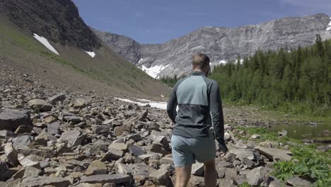 Hiker-walking-down-valley-by-pond-and-forest-close-up-followed-Rockies,-Kananaskis,-Alberta-Canada