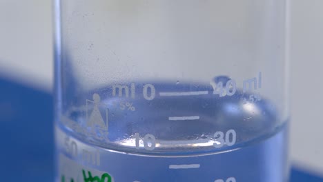 Close-up-of-clear-liquid-dripping-into-a-chemistry-test-tube,-marked-with-measurements