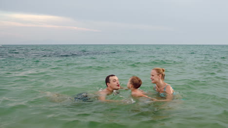 happy family of three playing ball in sea