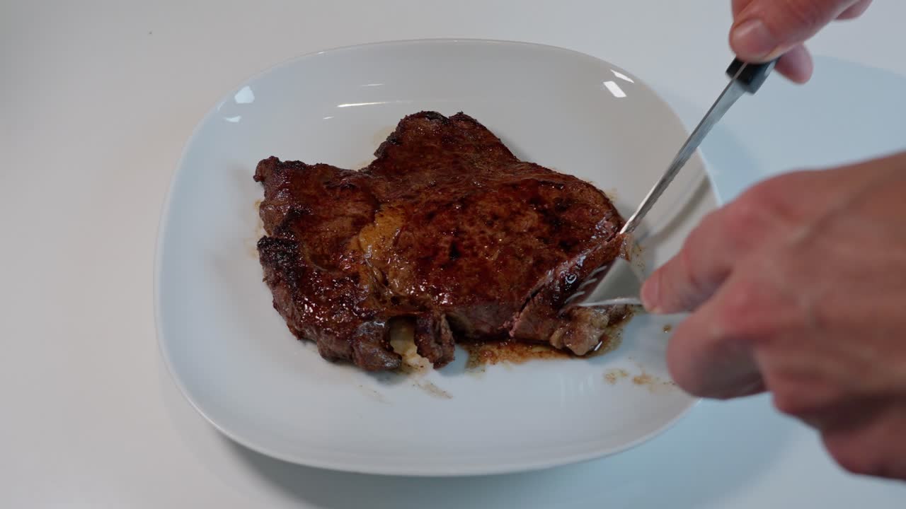 Ripresa dall'alto di entrecôte a media cottura su un piatto bianco, tagliata con forchetta e coltello per mostrare la carne succosa